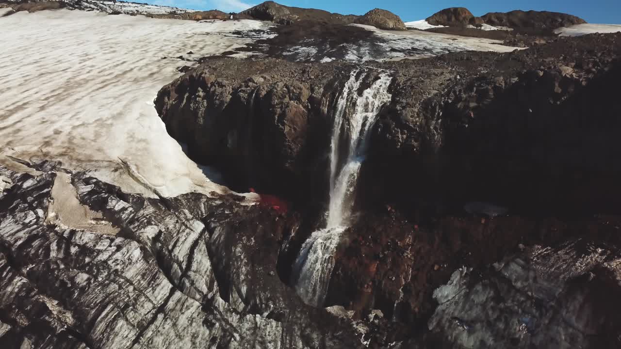 Letecký panoramatický pohled na ledovcovou řeku padající vodopádem před islandským ledovcem, za slunečného dne.