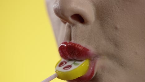 Mujer-Lamiendo-Paletas,-Lamiendo-Labios-De-Lápiz-Labial,-Primer-Plano-De-La-Boca-Sobre-Fondo-Amarillo