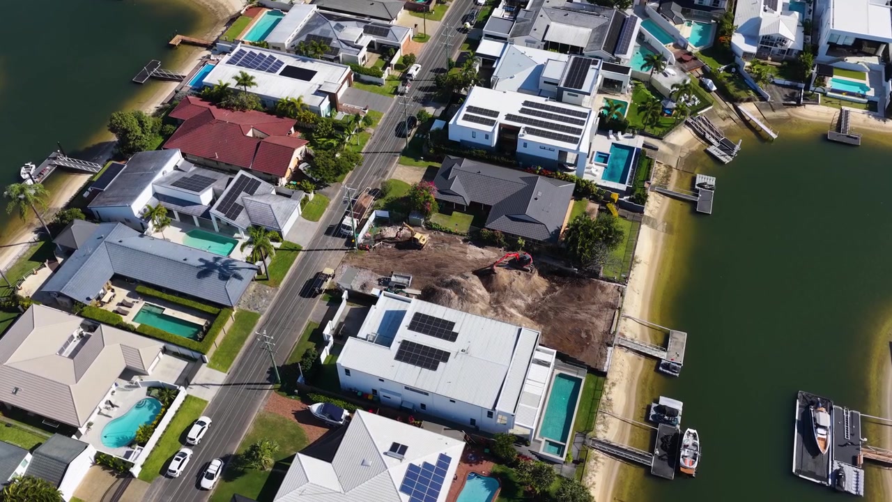 High-angle drone shot captures modern coastal residences, solar panels, and active construction along waterways.
