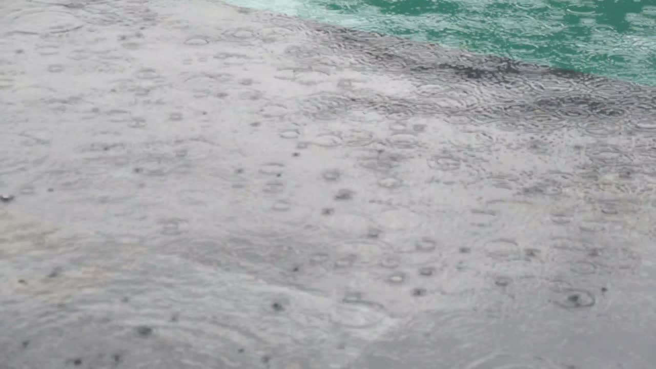 Tropical summer rain splashing into swimming pool. Close up of swimming pool during storm and rain drops falling into water.
