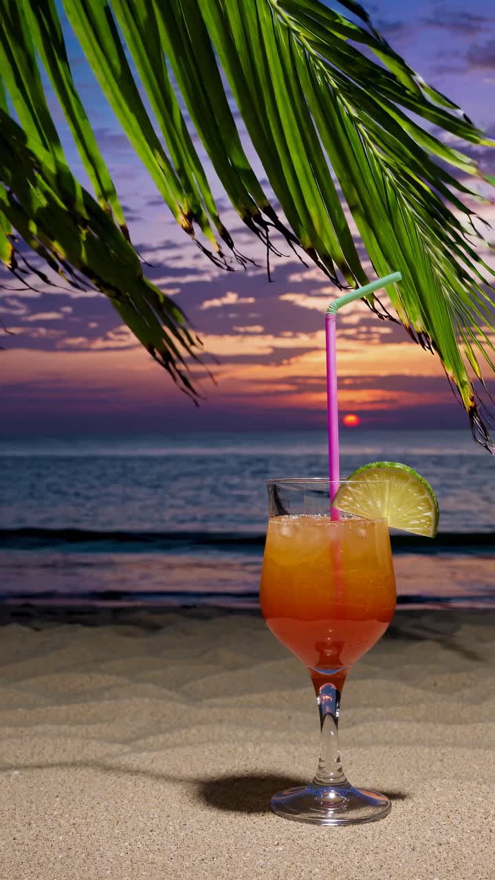 Tropical cocktail on sandy beach at sunset, framed by palm leaves