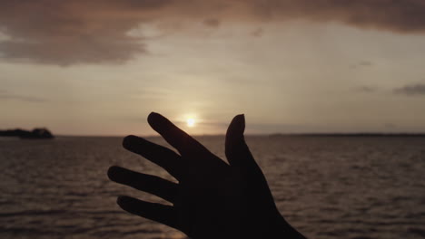 silhouette of a hand in front of the sunset at the pacific coast in buenaventura, colombia