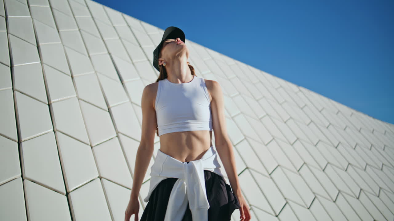 Sport girl stretching neck enjoying summer sunlight at urban architecture