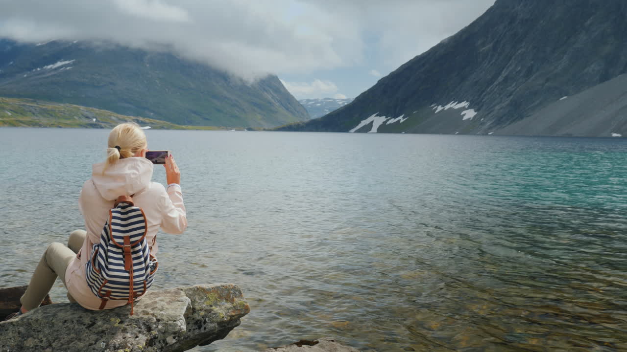 una mujer toma una foto de una vista panorámica de un lago noruego de alta montaña vacaciones en el borde o