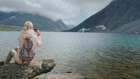 a woman takes a picture of a scenic view of a high-mountainous norwegian lake holidays at the edge o