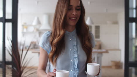 Happy-woman-bringing-tea-cups-to-husband-at-home.-Couple-having-coffee-break