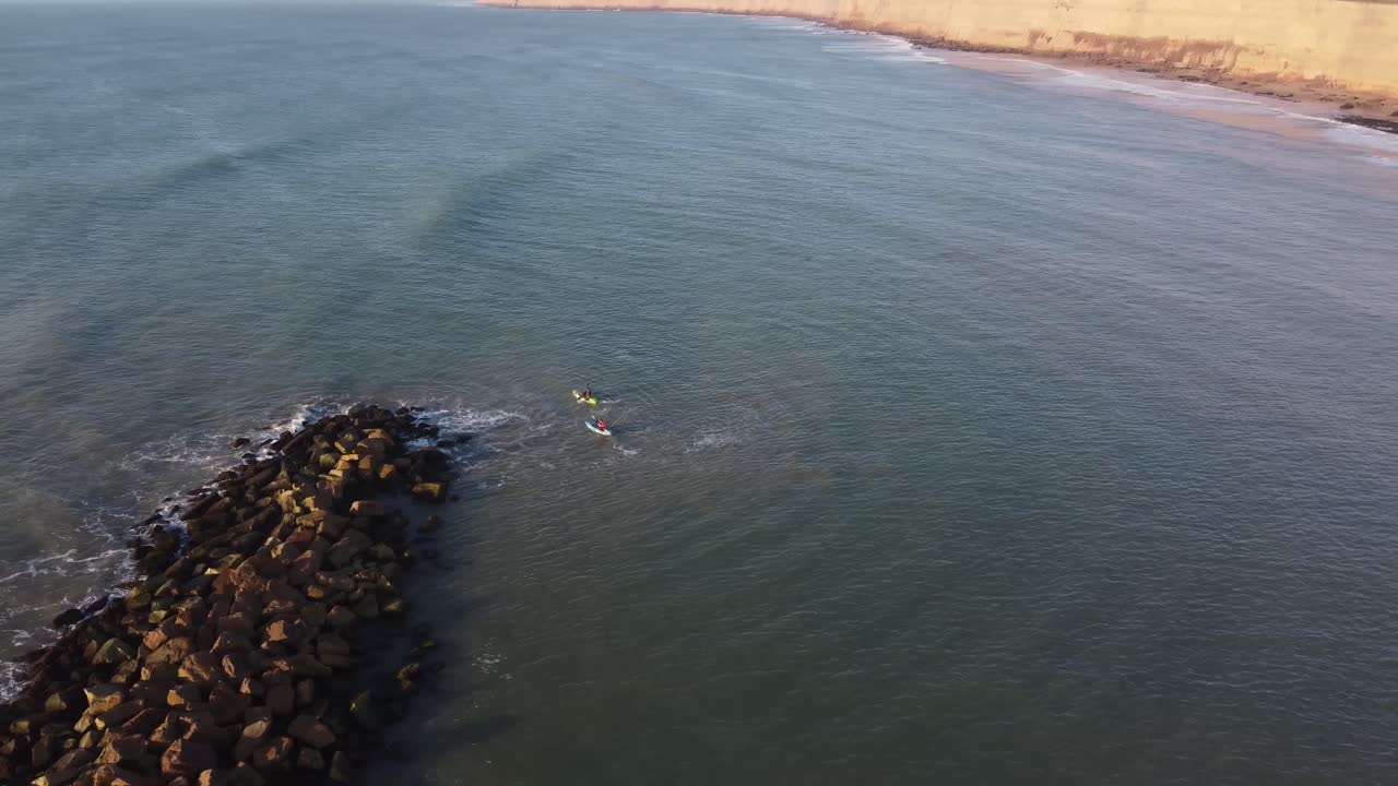 equipo de kayak remando en el amplio océano atlántico contra las olas del rompeolas durante la puesta de sol - toma aérea en órbita