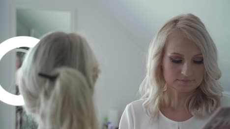 blonde woman getting her makeup done by a makeup artist