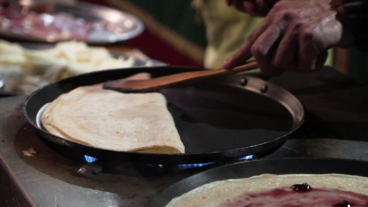 Folding a pancake in top of a pan in slow motion in a street market