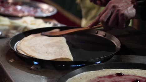 folding a pancake in top of a pan in slow motion in a street market