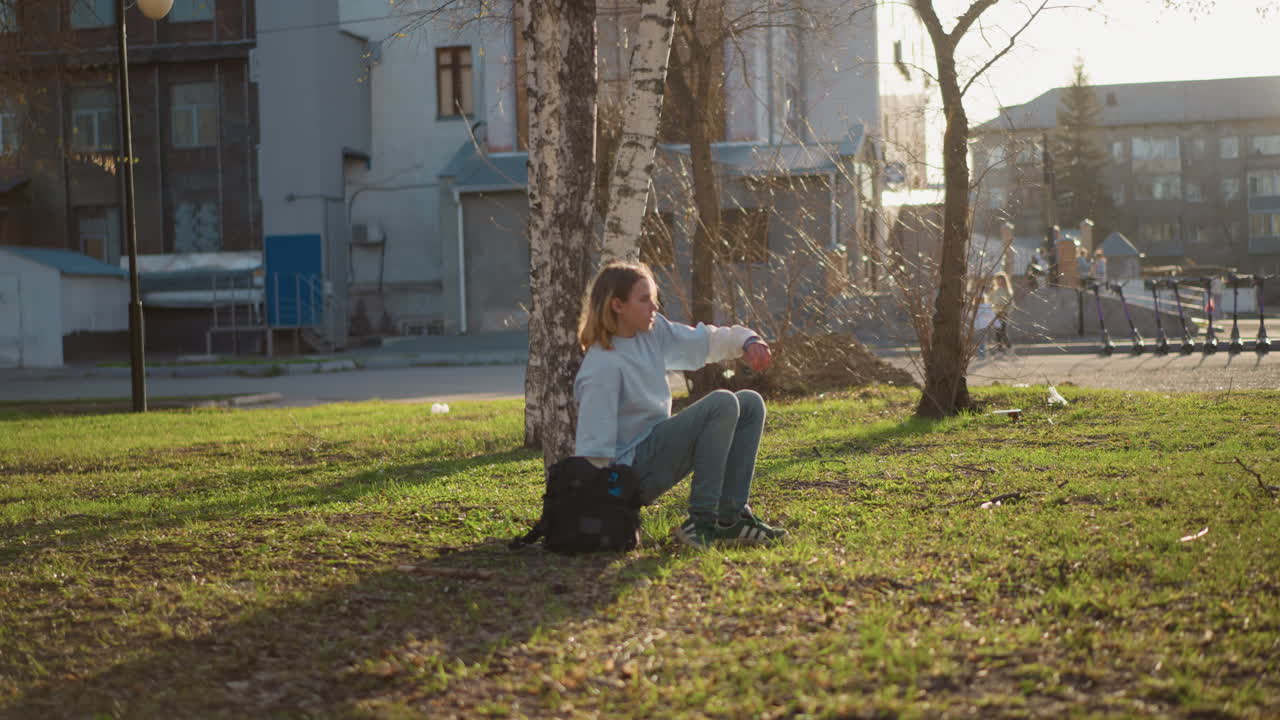혼자서 야외를 걷는 사람, 도시를 배경으로 자연 속을 홀로 거니는 여성, 햇볕이 잘 드는 풀이 무성한 도시 공원에서 나무 사이를 한가로이 거닐고 있는 외로운 여성