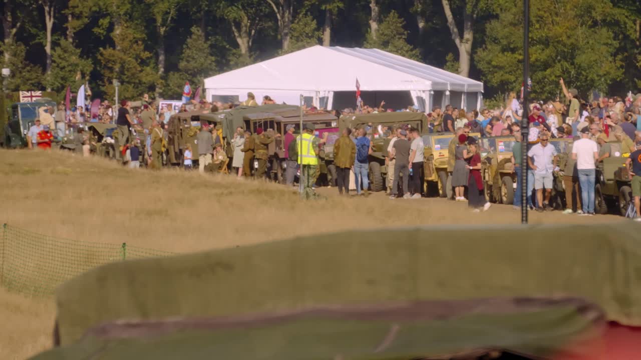 Military parade scene with vintage vehicles and crowds gathered at an outdoor event in Ginkelse Heide, Ede, Netherlands. Soldiers in uniform and spectators participate in the historical reenactment