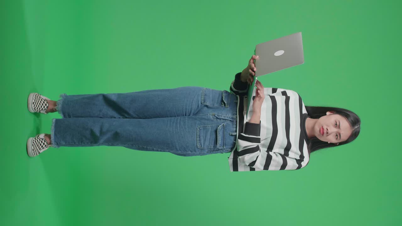 cuerpo lleno de mujer insatisfecha escribiendo en la computadora mientras está de pie frente al fondo de la pantalla verde