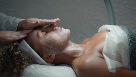 cosmetologist hands massaging face with nourishing cream in spa salon closeup.