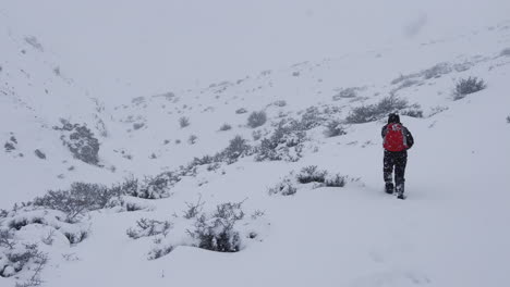 un hombre con una mochila roja caminando por las montañas, en una tormenta de nieve, montaña cubierta de nieve