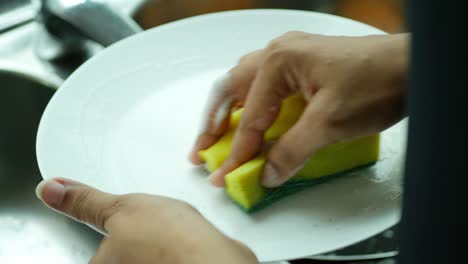 Women-hand-cleaning-a-white-plate-with-sponge-,