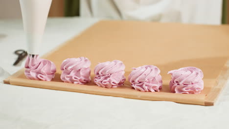 close up of cupcake preparation process showing piping bag forming delicate swirls of pink dough on brown baking paper, neatly arranged in a row for baking