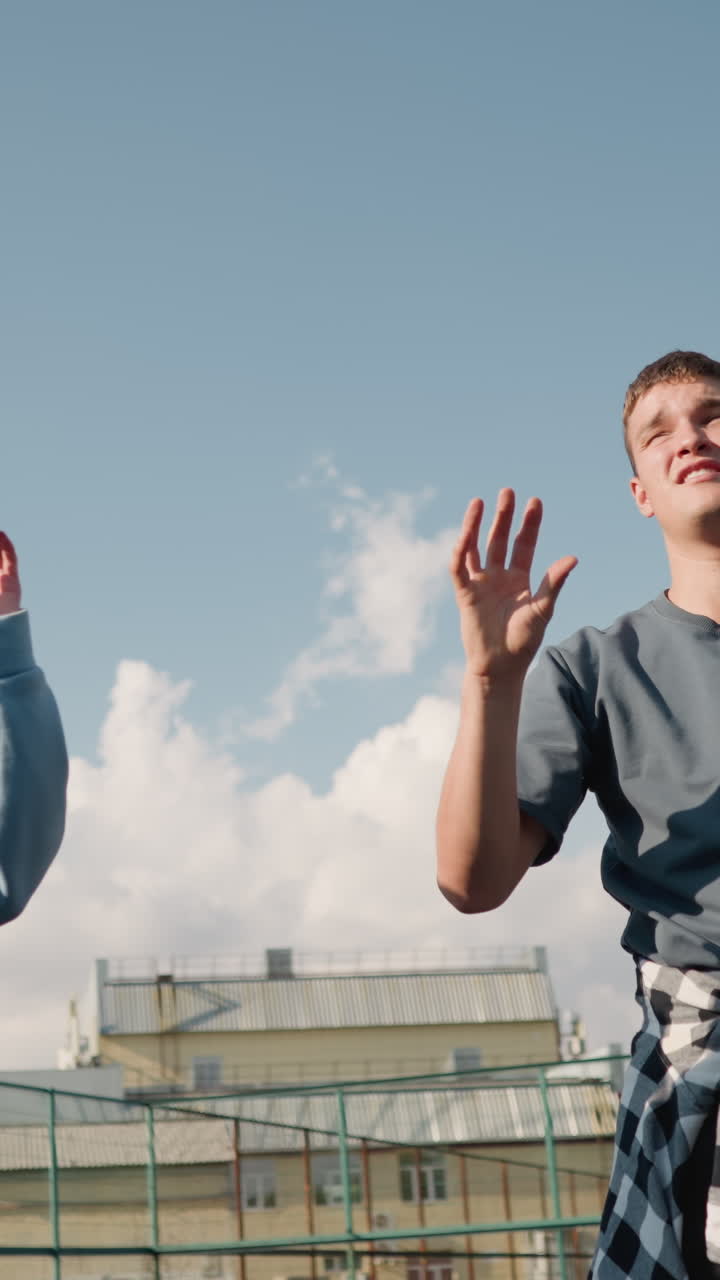 sesión de entrenamiento de principiantes jugando voleibol con un entrenador que lleva una camisa a cuadros alrededor de la cintura en una cancha abierta, el fondo presenta un edificio y una valla, practicando técnicas de voleibol