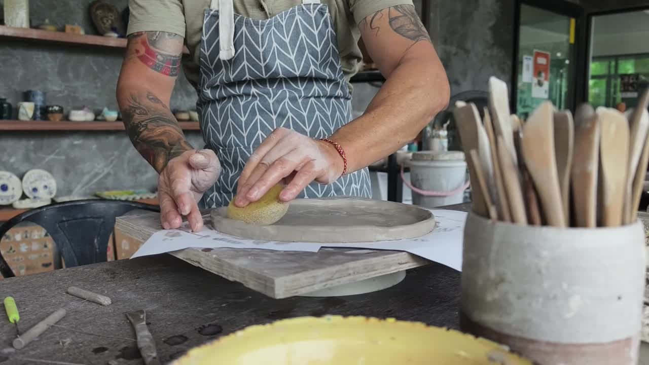 Craftsman Smoothing Clay Plate with Sponge in Pottery Workshop