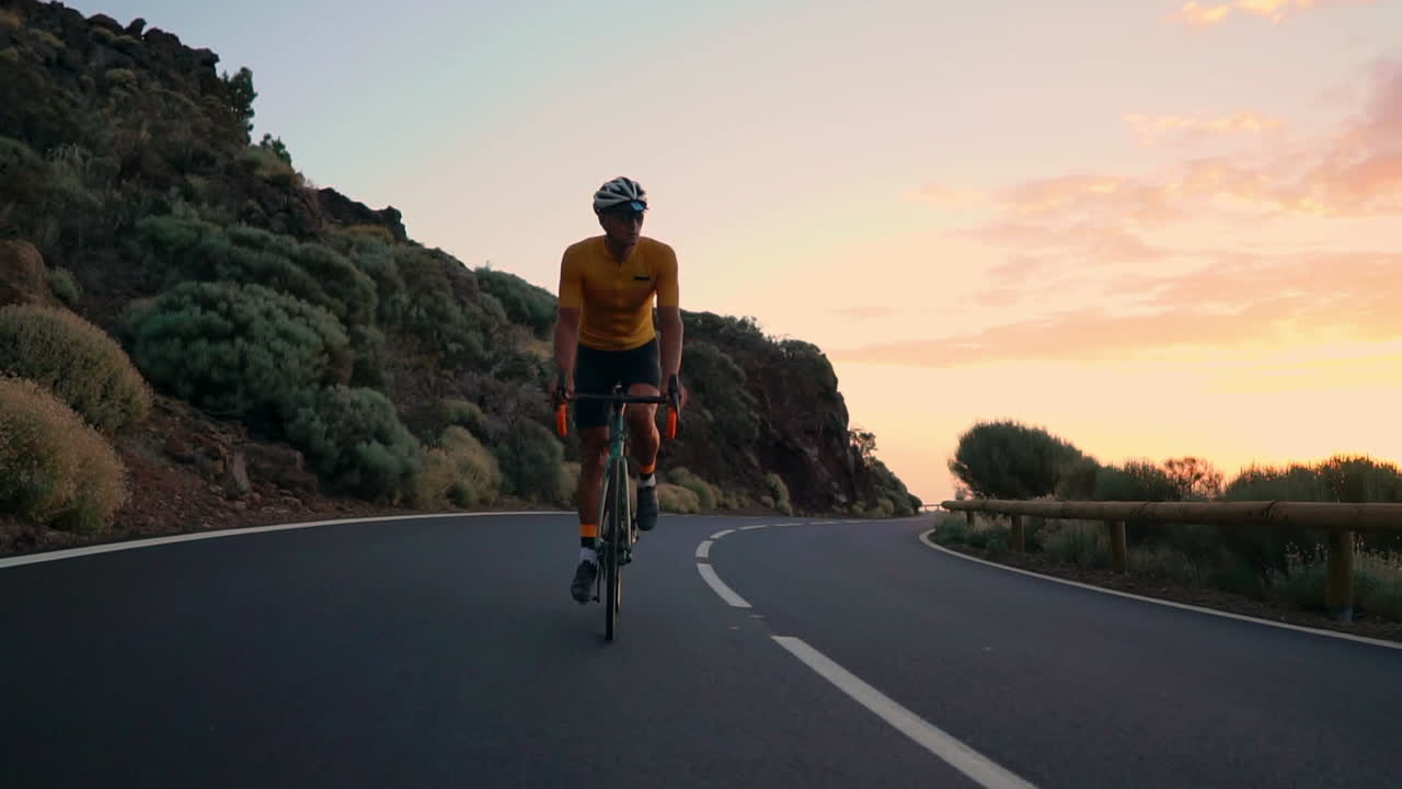In slow motion, the athlete cycles on a mountain serpentine, embracing the island's view, symbolizing a dedication to a healthy lifestyle during sunset