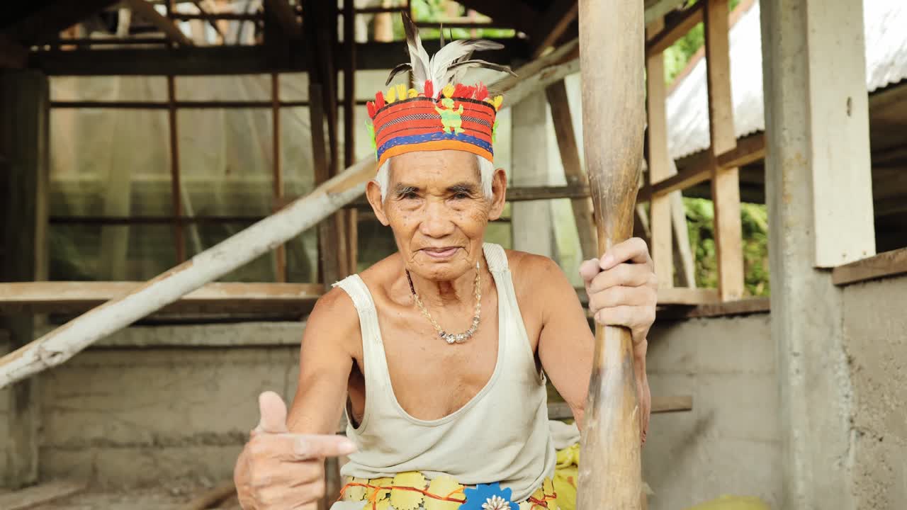 Agricultor filipino de frente para a câmera segurando um pilão de madeira e fazendo gesto de apontar