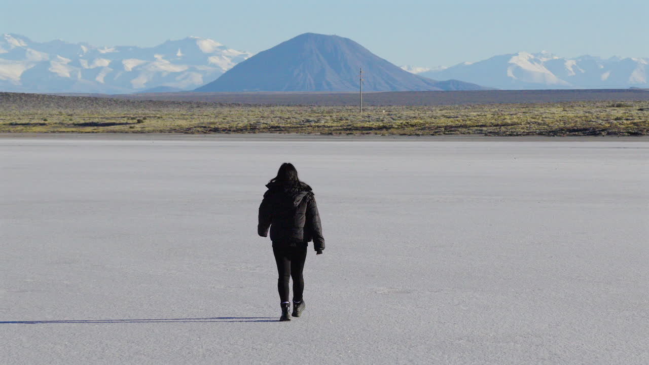 Woman walking alone across salt flat with Andes mountains in the background, solitude and adventure