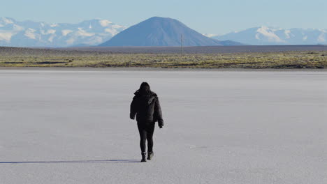 woman walking alone across salt flat with andes mountains in the background, solitude and adventure