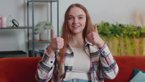 Una-Mujer-Joven-Y-Bonita-Mirando-La-Cámara-Levanta-Los-Pulgares-Y-Está-De-Acuerdo-Con-Algo-Positivo-Y-Bueno-En-Casa