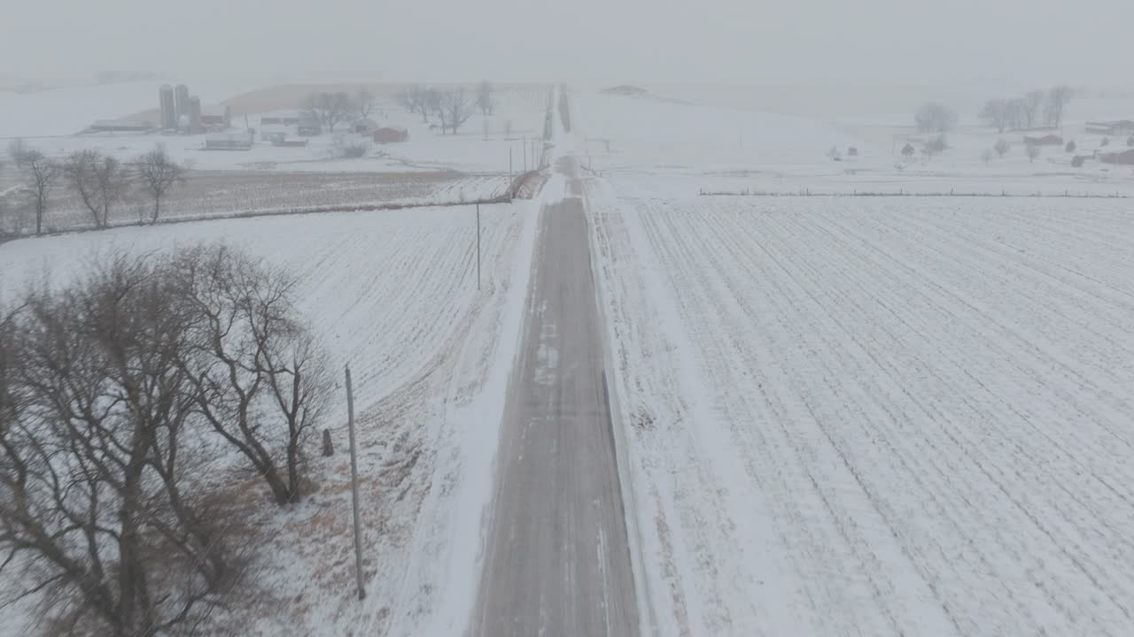Aerial moving shot of through rural country road covered in snow during blizzard.