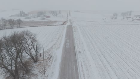 aerial moving shot of through rural country road covered in snow during blizzard.