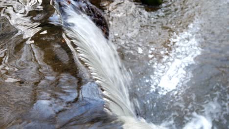 closeup on small flowing copper woodland river cascading into waterfall dolly left from above