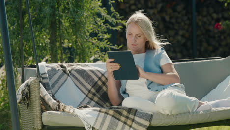 happy woman uses a tablet. resting in a garden swing in the backyard of a house