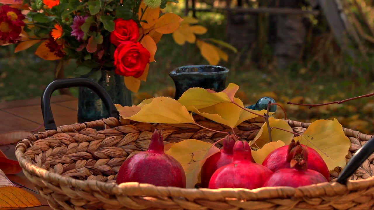 Melograni rossi maturi in un cesto su un tavolo da giardino con un bouquet di fiori in un vaso sullo sfondo.