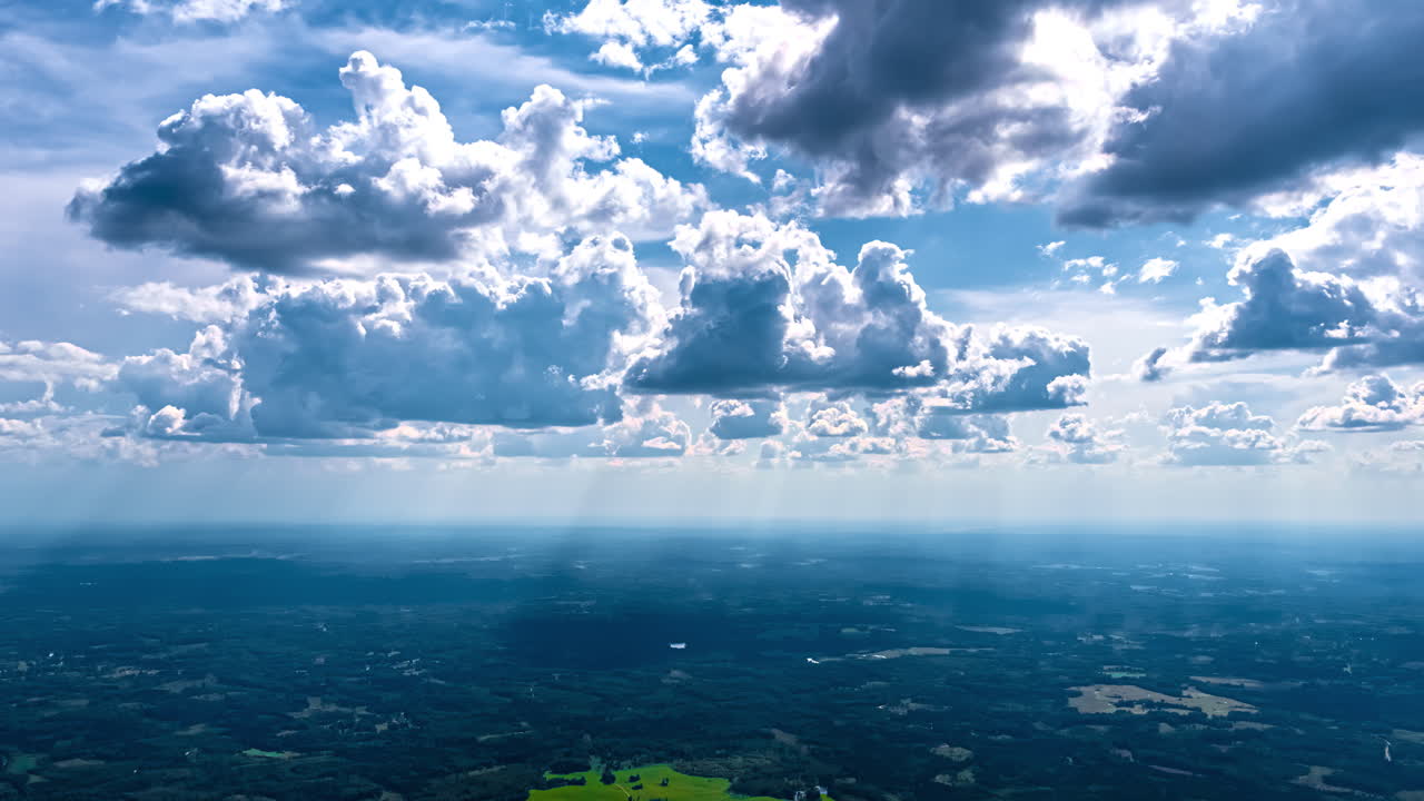 Clouds drifting over green fields and rolling hills with stunning rays of light descending across the landscape