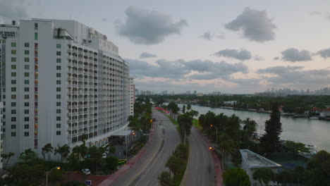 Forwards-fly-above-multilane-road-leading-through-tropical-city.-Palm-trees-waving-in-wind-at-dusk.-Aerial-view-of-modern-borough-with-multistorey-buildings.-Miami,-USA
