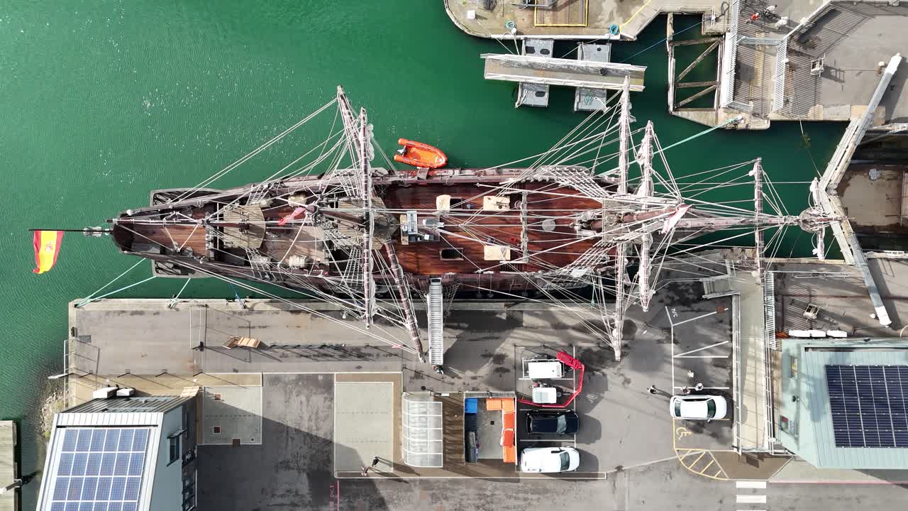 Stunning aerial shot of a historic replica Spanish galleon moored at modern Harbour. Unique perspective highlighting sails, rigging, and dramatic harbour backdrop
