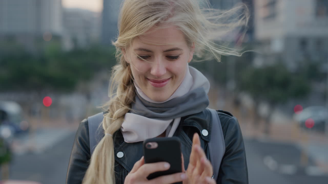 portrait beautiful young blonde woman using smartphone enjoying reading text messages browsing on mobile phone in city at sunset