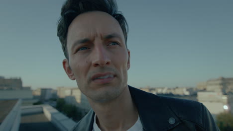 Close-up-of-face-of-young-troubled-man-smoking-on-roof-in-city-in-evening-sun