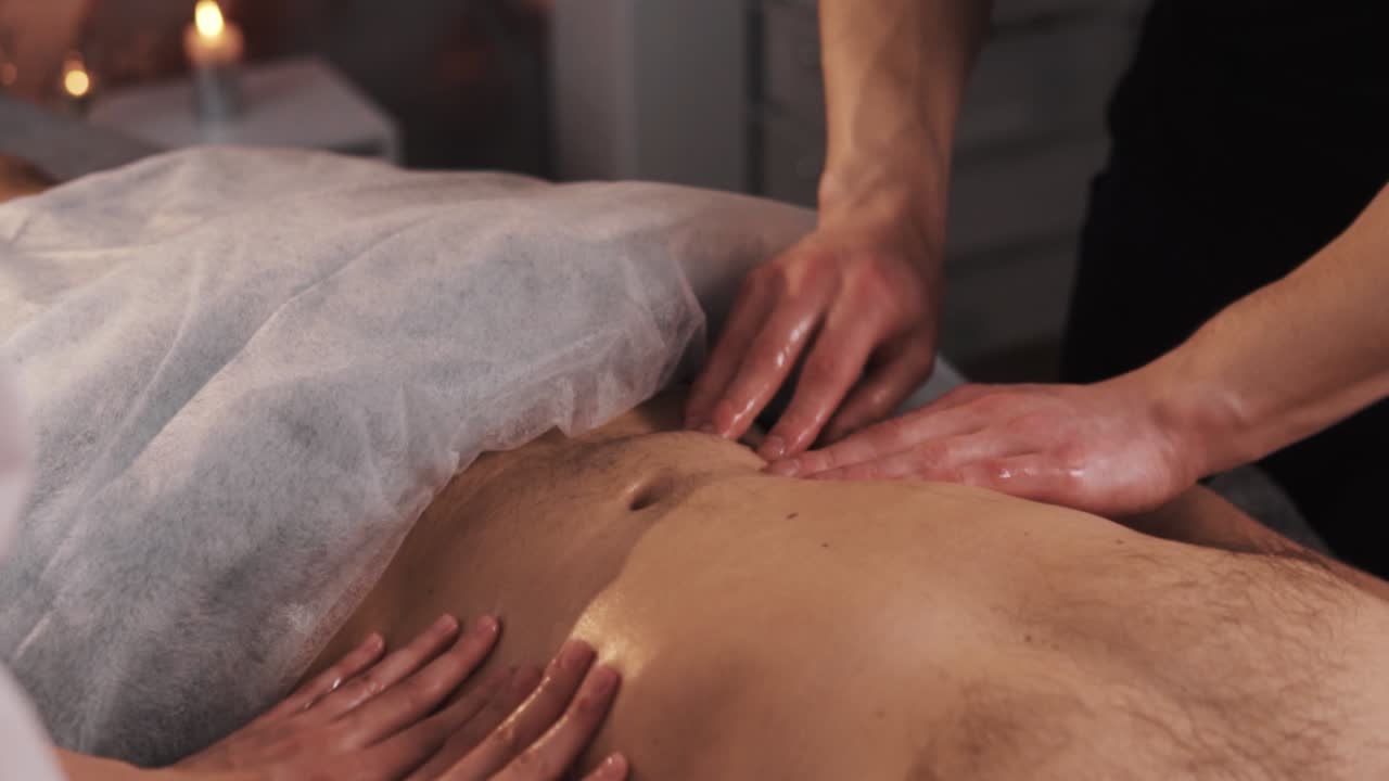 manos de una mujer y un masajista masajean el abdomen en cuatro manos de un hombre con físico deportivo