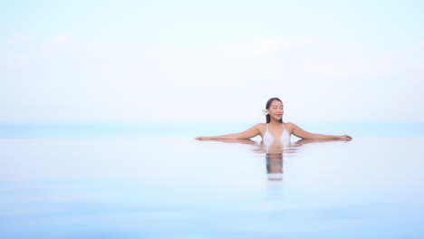 foto clave alta de una hermosa mujer asiática con flores en el cabello relajándose en la piscina infinita