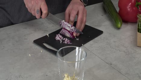 Red-onion-is-diced-on-cuttingboard,-garlic,-pepper,-cucumber-nearby