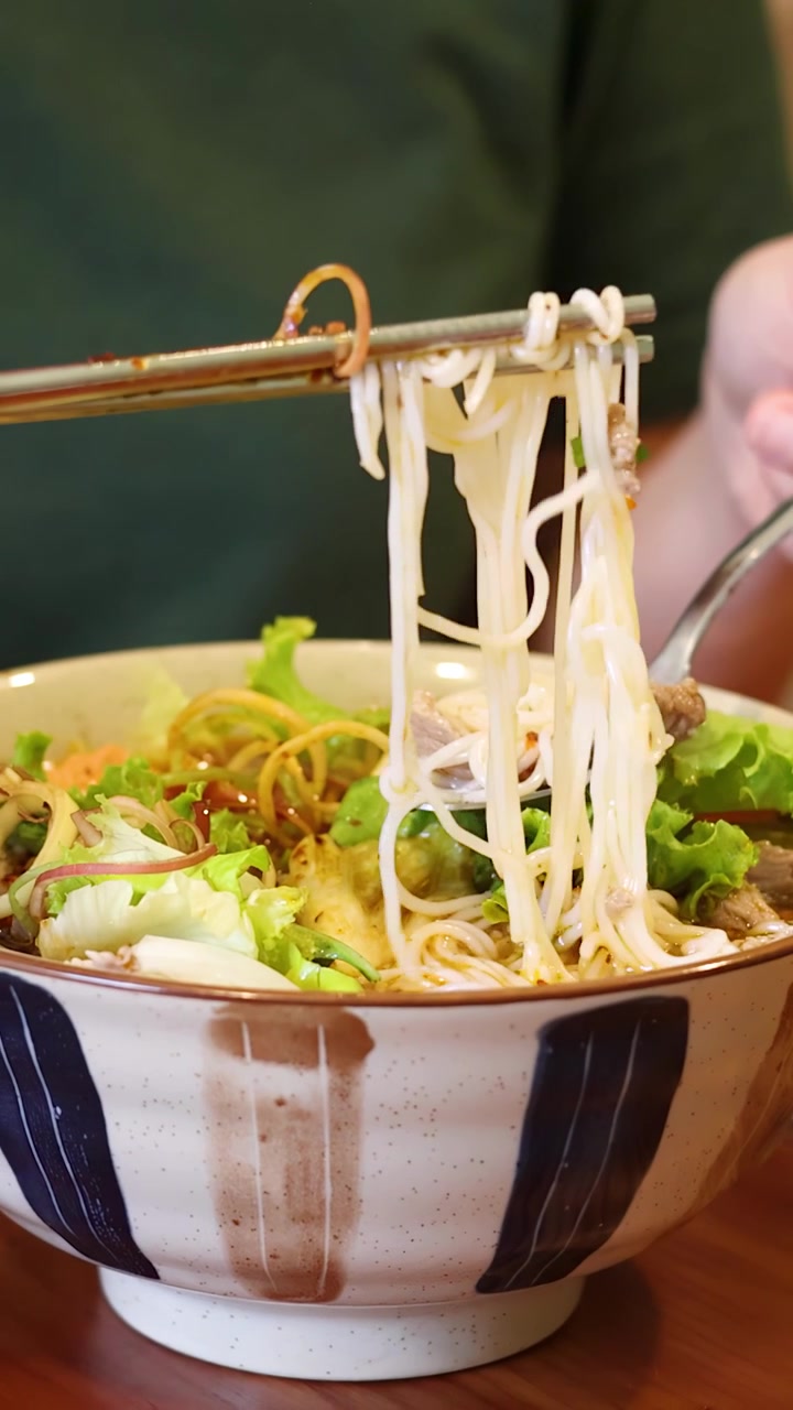 Primo piano di una persona che usa bacchette e un cucchiaio per mangiare bun cha vietnamita.
