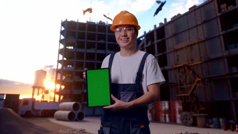 un trabajador asiático muestra una tableta de pantalla verde a la cámara en el sitio de construcción