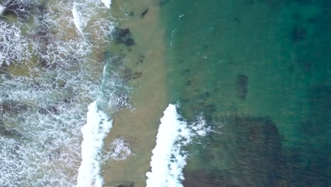 top down waves at a beautiful ocean coast - drone shot rocks and blue green waves