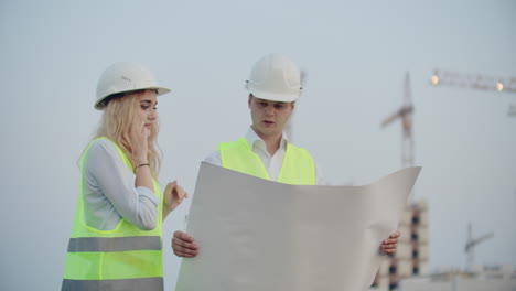 two engineers discuss looking at the drawings of the construction plan and the location of the objects specifying the contractor on the phone details. talking on the phone at the construction site.