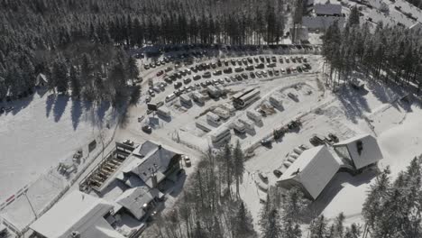 Kope-winter-resort-and-RV-car-parking-lot-in-the-Pohorje-mountains-Slovenia-with-snowy-roofs,-Aerial-pan-left-shot