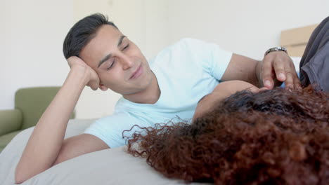 Happy-diverse-gay-male-couple-lying-on-bed-embracing-and-talking-at-home,-slow-motion