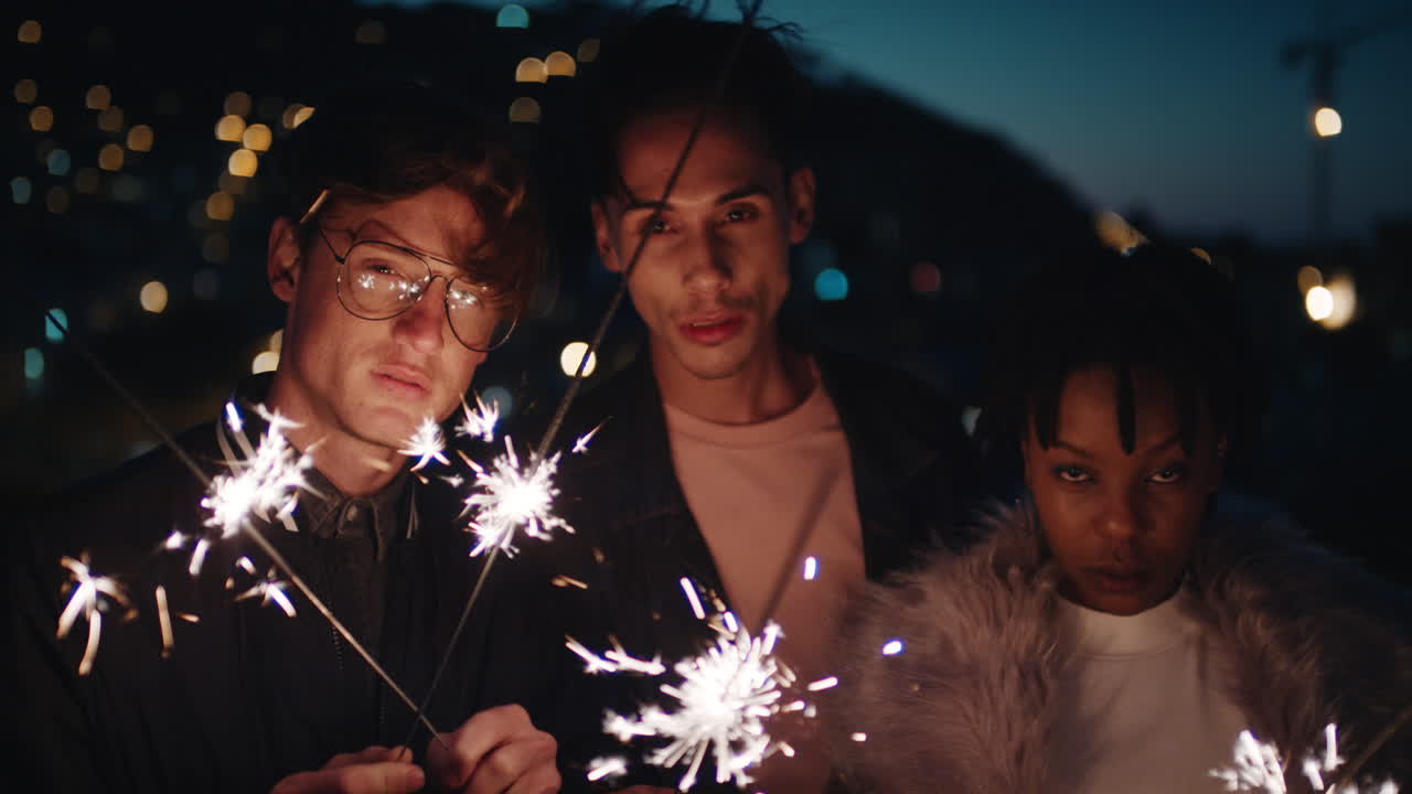 gruppo di amici che tengono stelle filanti che festeggiano il capodanno sul tetto di notte in posa con le bellissime luci della città sullo sfondo