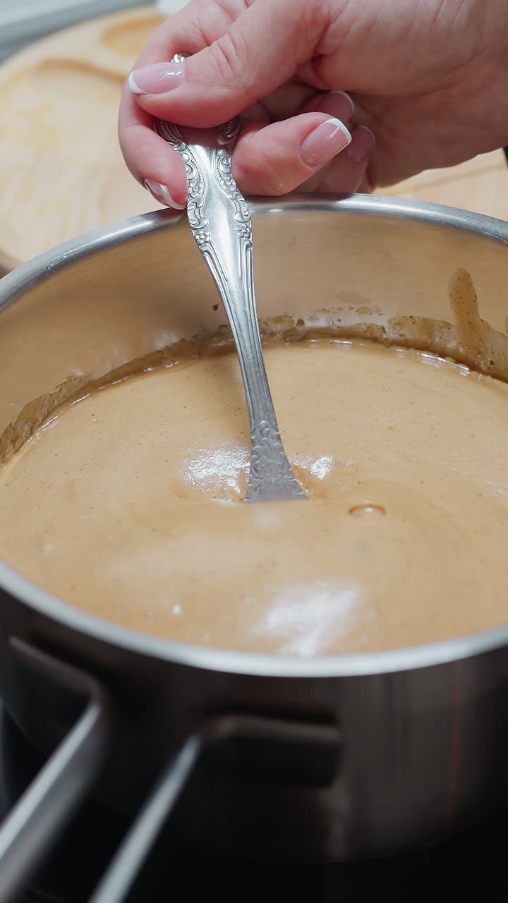 persona sosteniendo una olla en la estufa eléctrica mientras agita la avena gruesa mientras burbujea debido al calor, vista parcial de un plato blanco con mantequilla y tabla de madera en la encimera oscura en un entorno de cocina moderno