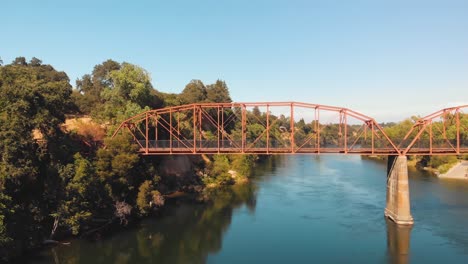 Drone-Volando-Sobre-El-Río-Americano-Hacia-El-Puente-Red-Fair-Oaks-Mientras-Un-Hombre-Cruza